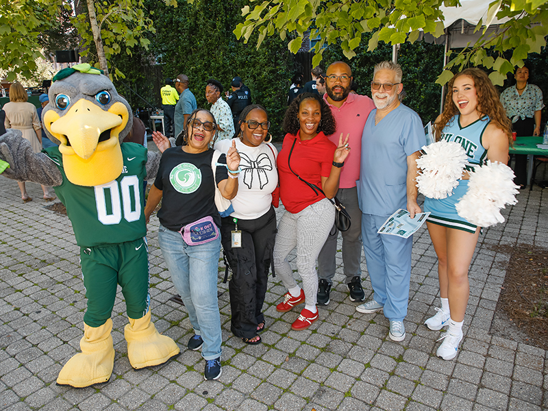 Riptide the pelican poses with a smiling group at commUNITY 2026.