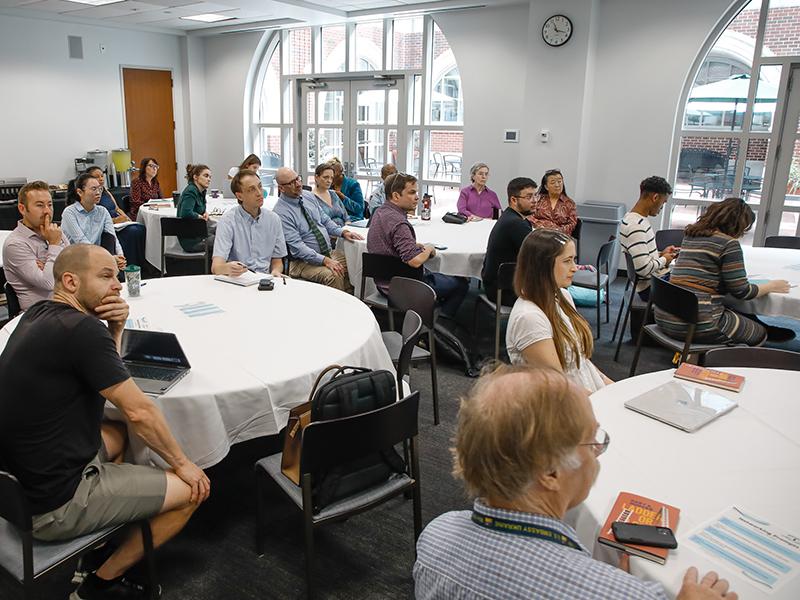 Tulane faculty, staff and students sit at round tables listening to a presentation.