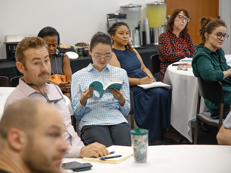 A Tulanian reads a book while others sit around her during a presentation.