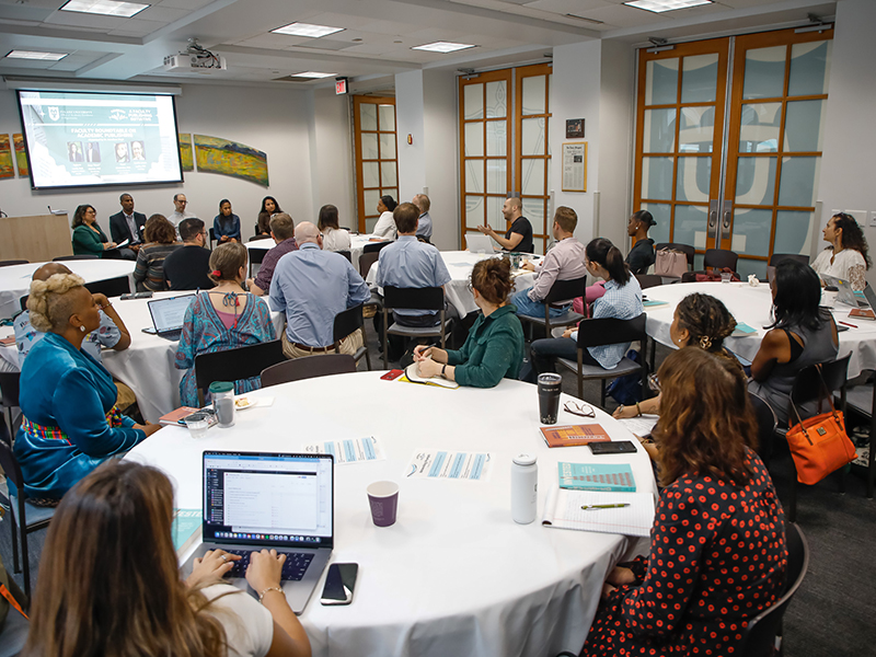 Tulanians gather around round tables to watch a panel discussion during a workshop.