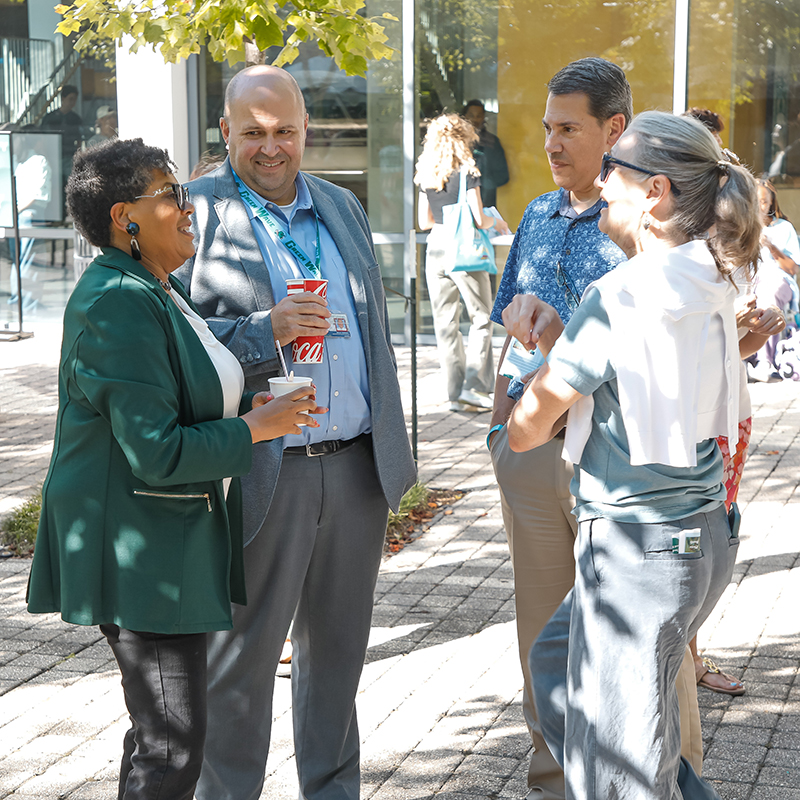 Faculty stand in a circle chatting at the 2026 commUNITY event.