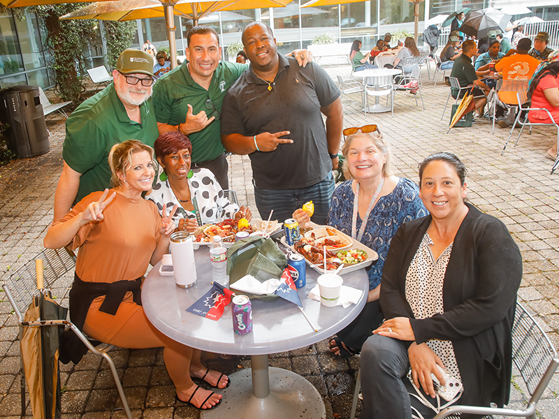 A group of Tulanians sit and stand around a table and smile at the camera during Juneteenth on Tulane's Uptown campus.