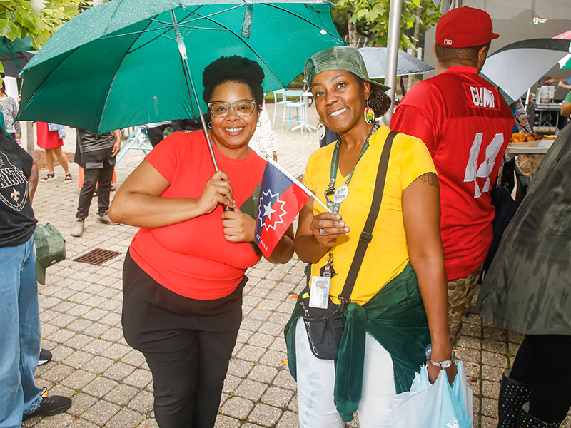 Two Tulanians hold umbrellas and smile at the camera during Juneteenth on Tulane's Uptown campus.