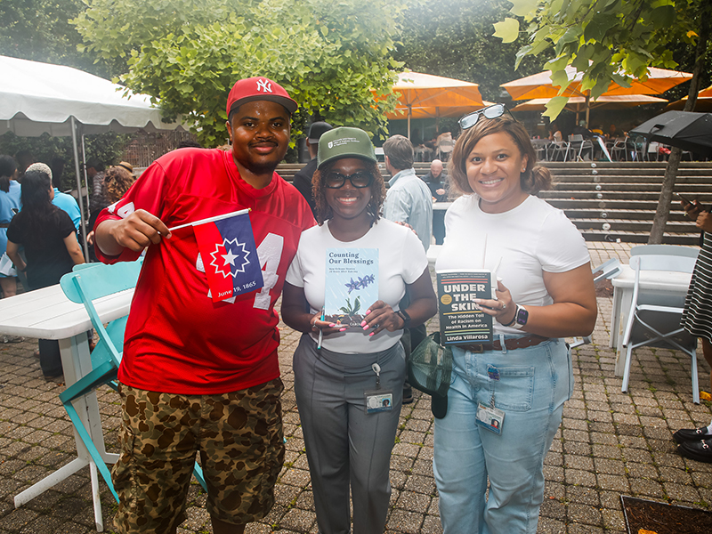 Three Tulanians holding books smile for the camera during Juneteenth on Tulane's Uptown campus.