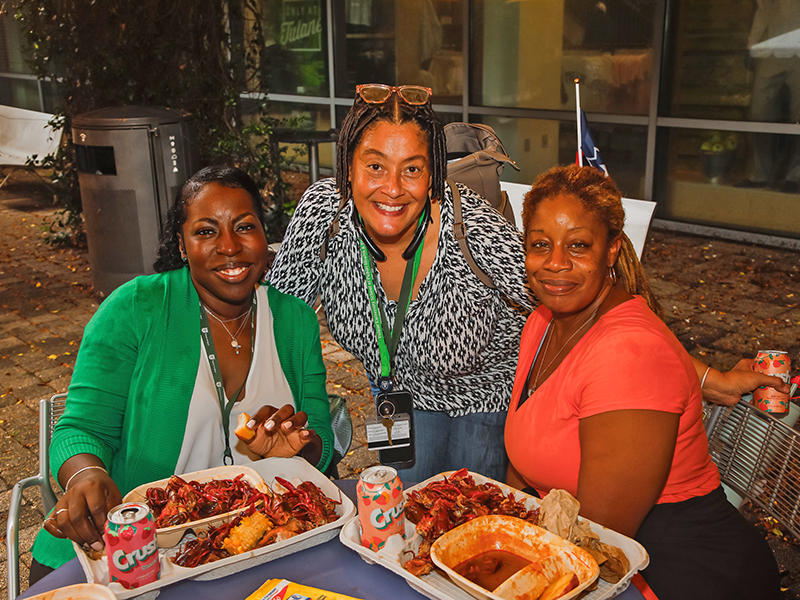 Three Tulanians smile at the camera as they sit around a table with boiled seafood during Juneteenth on Tulane's Uptown campus.