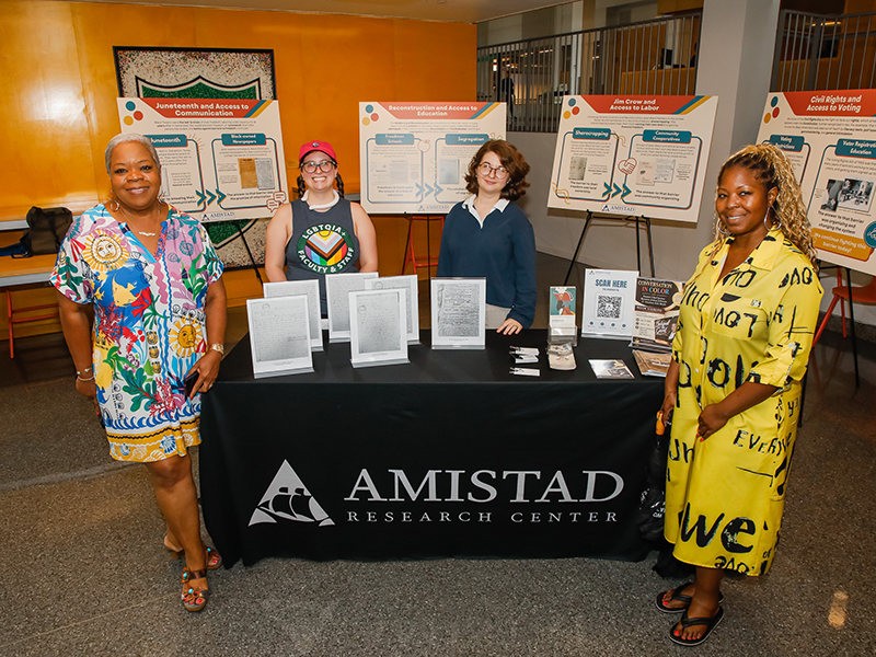 Four people pose around a table display from the Amistad Research Center during Juneteenth on Tulane's Uptown campus.