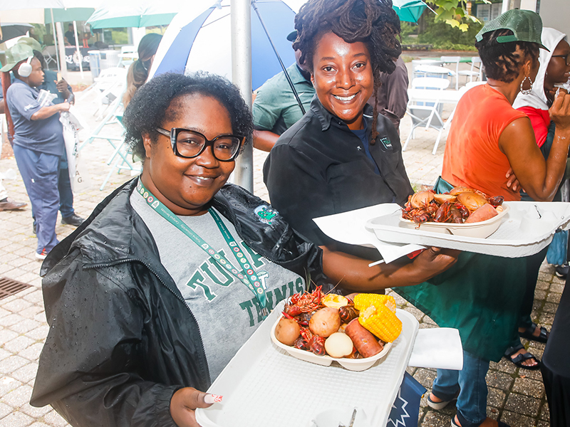Two Tulanians hold platters of boiled seafood and smile at the camera during Juneteenth on Tulane's Uptown campus.
