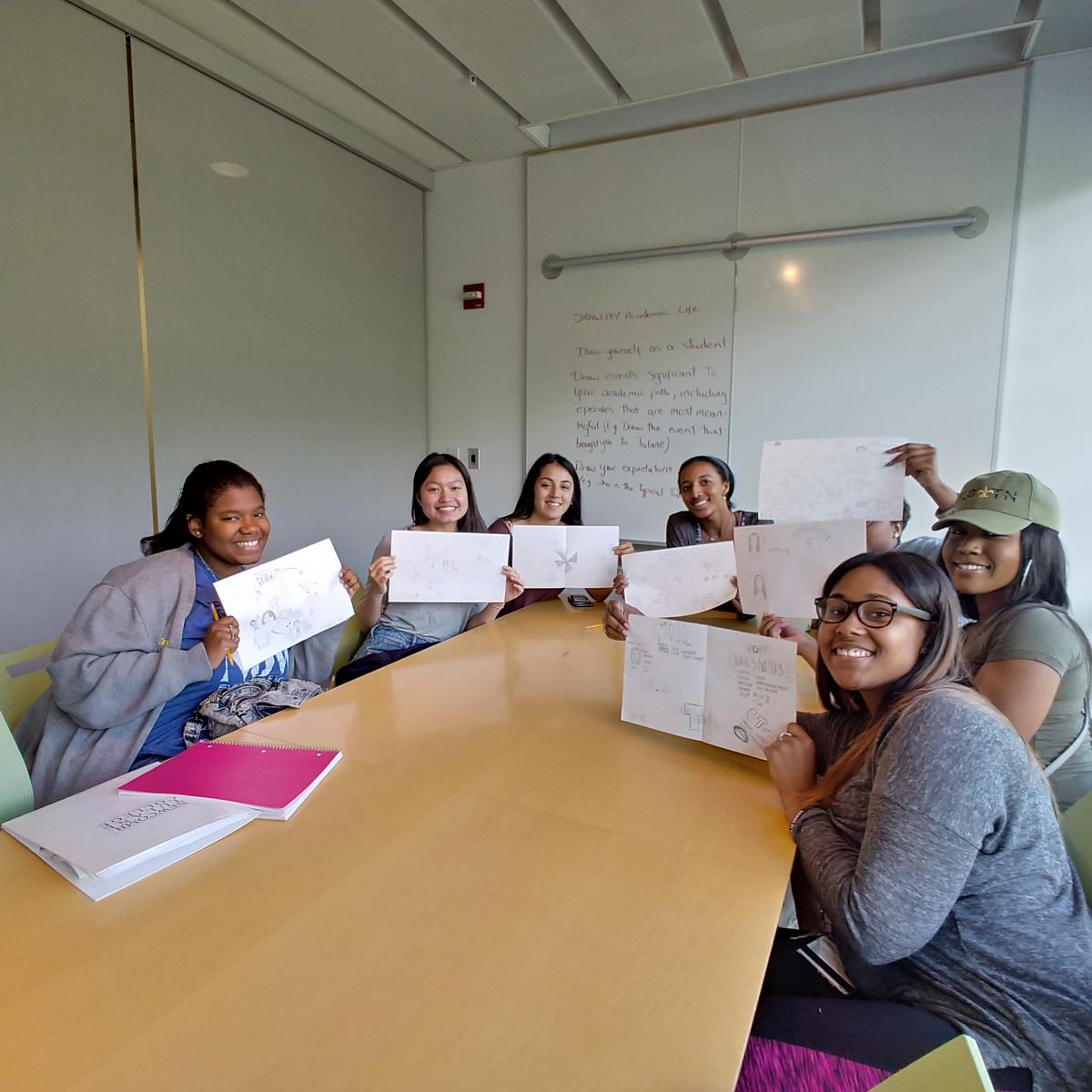 Tulane students sitting at a table holding papers up and smiling at the camera.